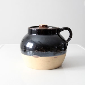 Puede incluir: Un tarro de cerámica vintage de color marrón y crema con tapa y asa.
