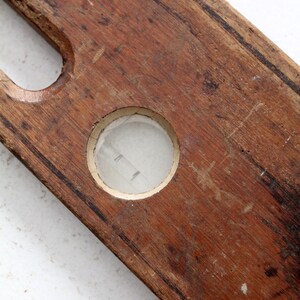 May include: A vintage wooden level with a circular glass bubble level. The level is made of dark brown wood and has a worn, aged appearance.