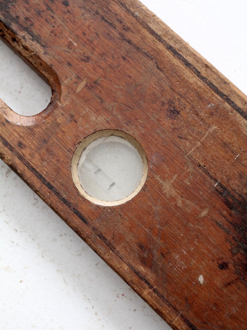May include: A vintage wooden level with a circular glass bubble level. The level is made of dark brown wood and has a worn, aged appearance.