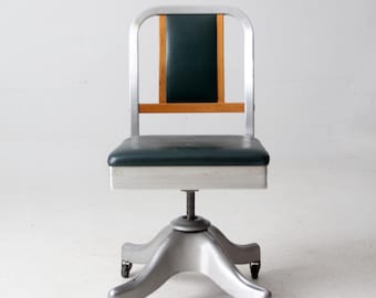 May include: Vintage office chair with a silver metal frame and a dark green seat and backrest. The backrest features a wooden accent. The chair has a five-star base with rolling casters.