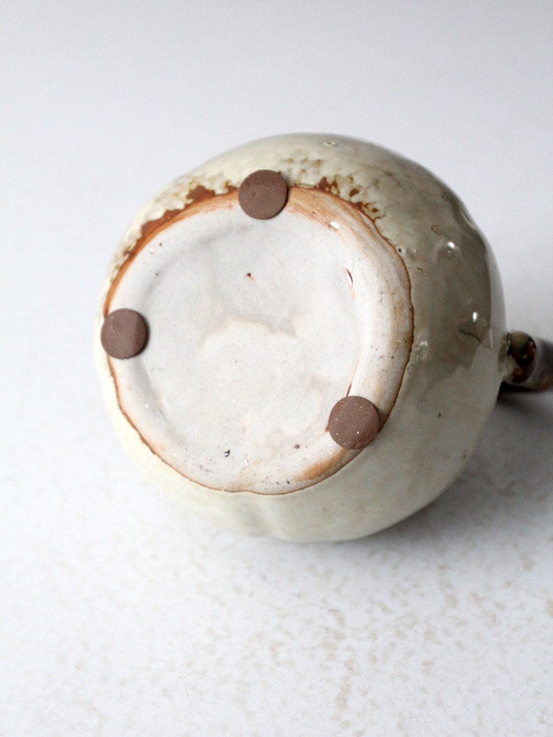 May include: The bottom of a ceramic pitcher with a light brown glaze and three brown rubber feet.