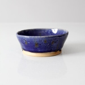 Könnte beinhalten: Eine kleine, handgefertigte Keramikschale mit tiefblauer Glasur. Die Schale hat einen hellbraunen Boden und ist mit geprägten Blumenmustern verziert. Das Innere der Schale ist glänzend blau, und die Außenseite hat ein leicht strukturiertes Aussehen.