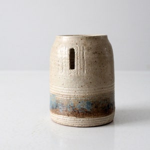 May include: A white ceramic vase with a blue and brown glaze. The vase has a rectangular opening on the side.