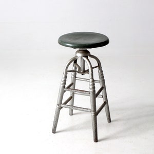 May include: A vintage adjustable metal stool with a green wooden seat. The stool has a silver finish and a simple design.