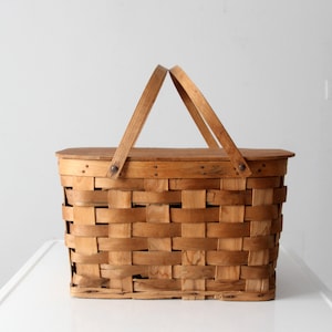 May include: A vintage wooden picnic basket with a woven design and a hinged lid. The basket has two wooden handles and is made of natural wood.