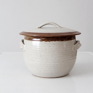 Könnte beinhalten: Weiße Keramik-Kanne mit braunem Rand und Deckel. Die Kanne hat zwei Griffe an den Seiten und einen einzelnen Griff auf dem Deckel.