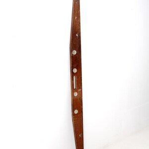 May include: A long, wooden level with five circular bubble levels. The level is brown and has a slight curve to it.