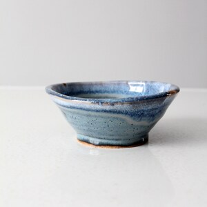 May include: A small, blue and brown ceramic bowl with a slightly uneven rim. The bowl has a speckled glaze and a light blue interior.