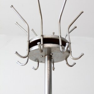 May include: A silver metal coat rack with a round base and multiple hooks. The rack is standing on a white surface.