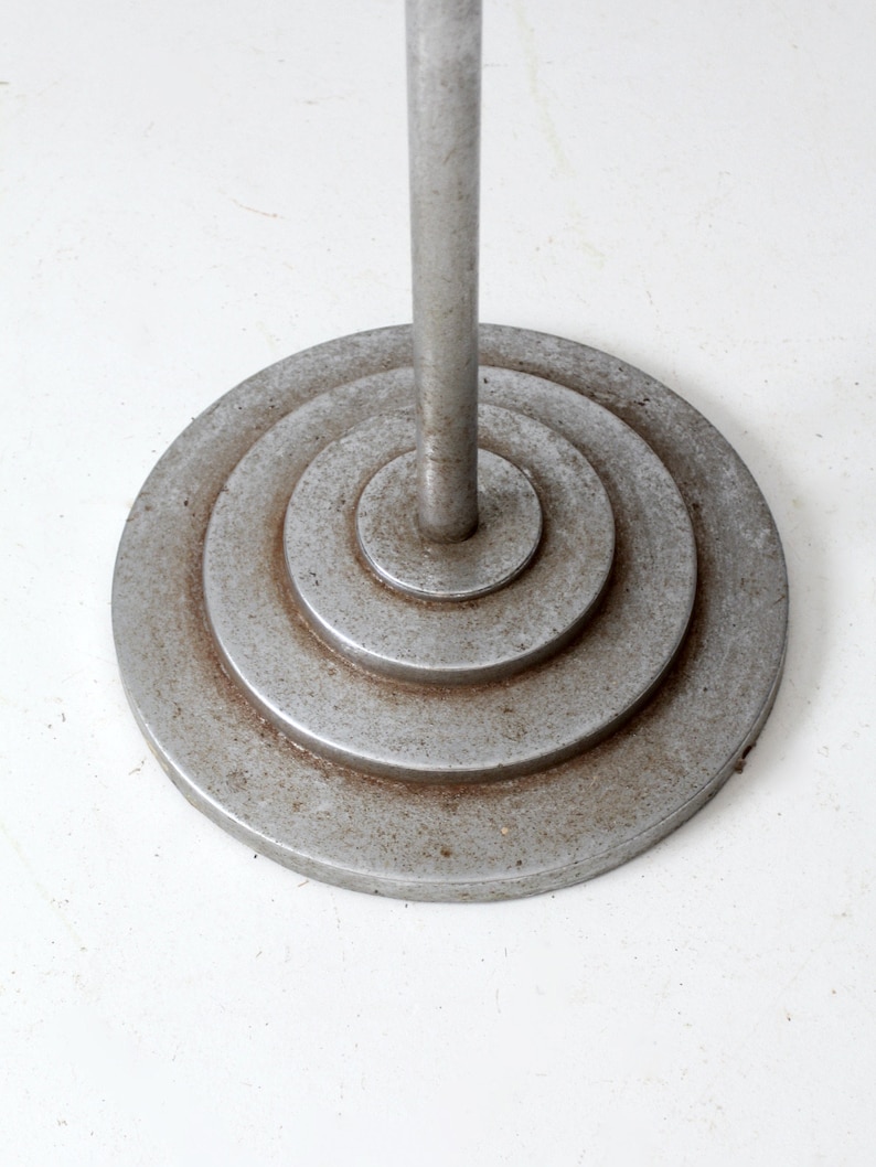 May include: A silver metal floor lamp base with a circular design. The base has concentric circles that create a layered effect.