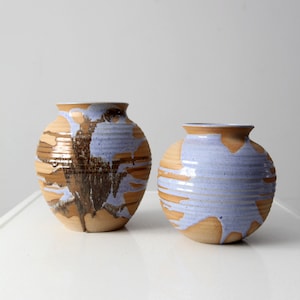Puede incluir: Dos jarrones de cerámica con un esmalte marrón claro y un esmalte azul claro. Los jarrones tienen una superficie texturizada, acanalada y una forma redondeada.