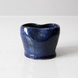 Peut inclure: Un petit pot en céramique bleu foncé avec un bord légèrement irrégulier et ondulé. Le pot a un glaçage moucheté et une finition brillante.
