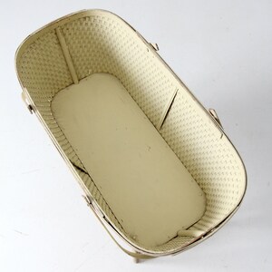 May include: A white wicker doll bassinet with a metal frame and handles. The bassinet is empty and has a white background.