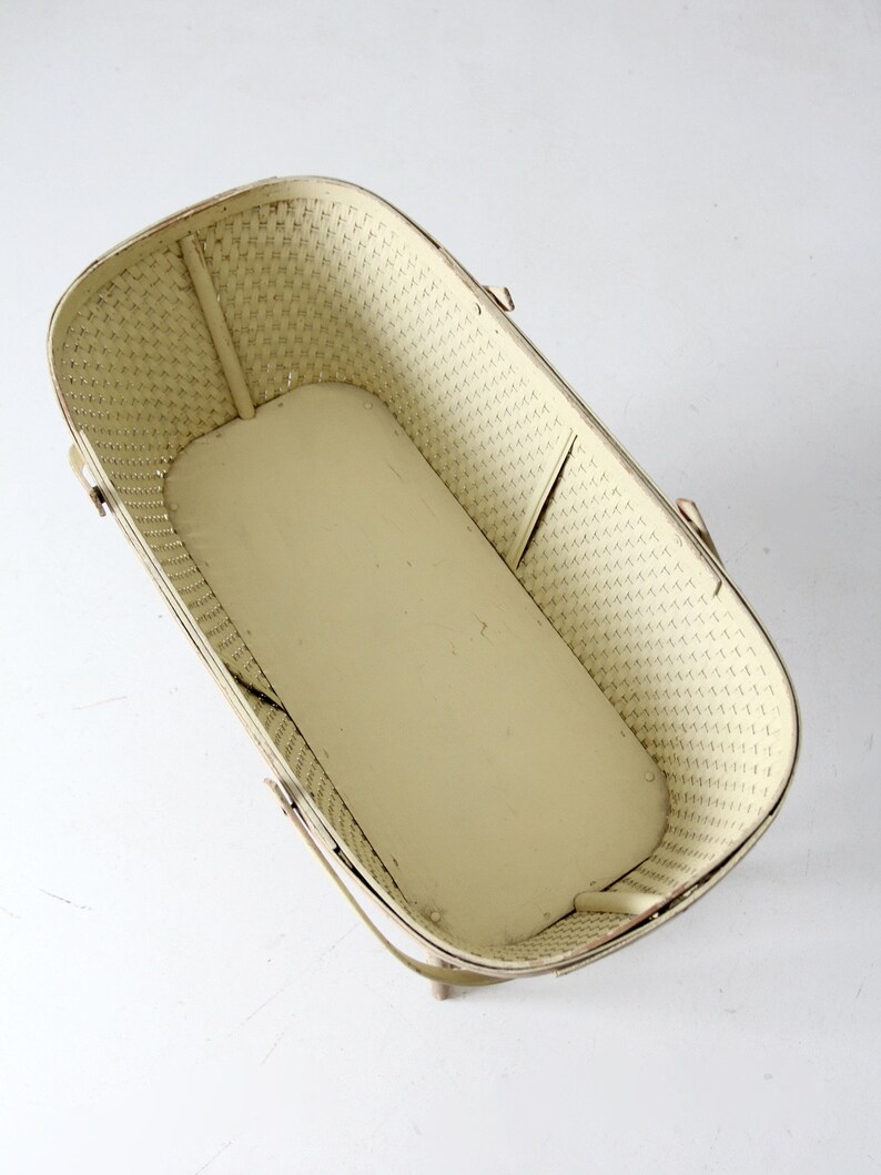 May include: A white wicker doll bassinet with a metal frame and handles. The bassinet is empty and has a white background.