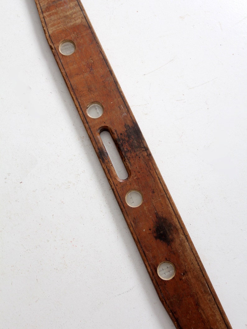 May include: A vintage wooden level with four glass vials. The level is brown and has a worn finish.