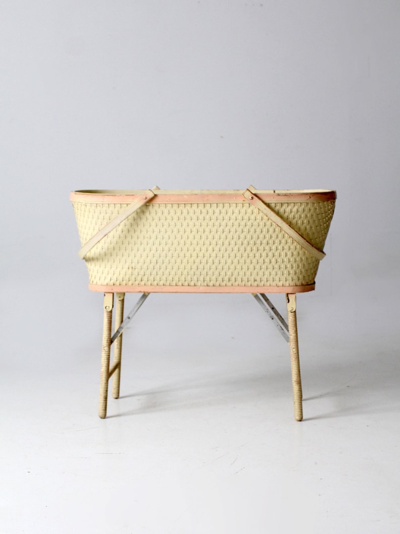 May include: A vintage wicker basket with a pink trim and wooden legs. The basket is empty and has two handles.
