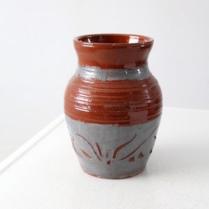 Pode incluir: Um vaso pequeno de cerâmica marrom com um esmalte cinza e um design decorativo. O vaso tem um corpo arredondado e uma abertura ligeiramente alargada.