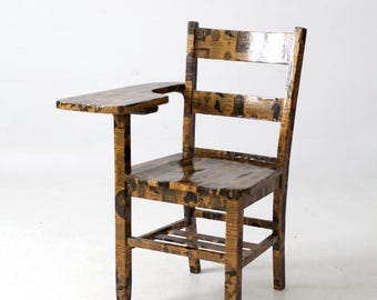 May include: Vintage wooden school chair with a built-in writing surface. The chair is covered in a newspaper print design with black and brown tones. The chair has a classic design with a backrest and four legs.