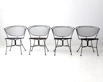 May include: Four black metal chairs with a wire mesh seat and back. The chairs are arranged in a row on a white surface.