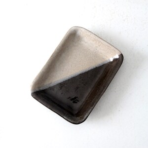 May include: A small rectangular ceramic dish with a diagonal line dividing the surface into two sections. One section is a light beige color and the other is a dark brown color.