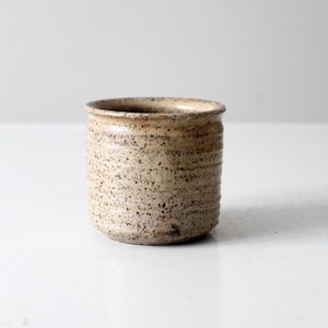 Peut inclure: Une petite tasse en céramique beige mouchetée avec un fond arrondi et un bord légèrement évasé.