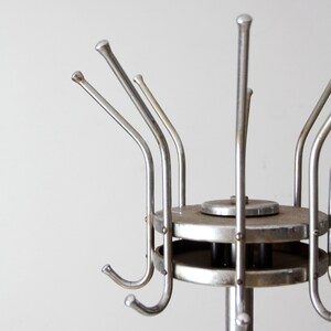 May include: A silver metal coat rack with multiple hooks. The rack has a round base and a tall, slender pole.
