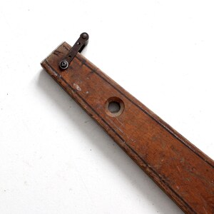 May include: A vintage wooden level with a metal lever and a hole in the center. The level is brown and has a dark brown stripe down the center.