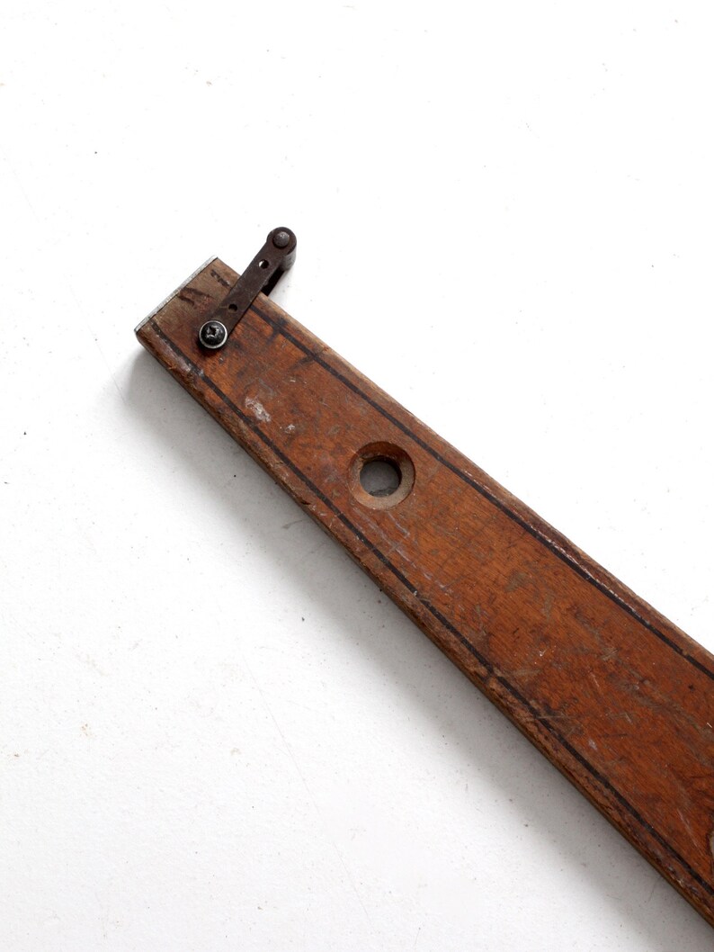 May include: A vintage wooden level with a metal lever and a hole in the center. The level is brown and has a dark brown stripe down the center.