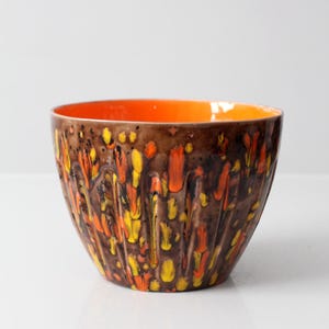 May include: A ceramic bowl with a brown exterior, decorated with orange and yellow dripped patterns. The interior is a solid orange. The bowl has a ridged texture.