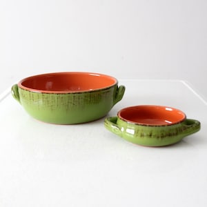 May include: Two ceramic bowls, one large and one small, with a green exterior and orange interior. Each bowl has two small handles. The green exterior has a textured appearance with dark brown accents.