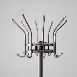 May include: A silver metal coat rack with a circular base and multiple hooks extending upwards. The hooks are arranged in a circular pattern around the base.