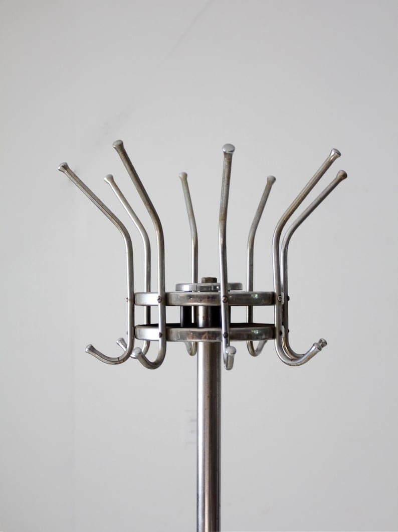 May include: A silver metal coat rack with a circular base and multiple hooks extending upwards. The hooks are arranged in a circular pattern around the base.