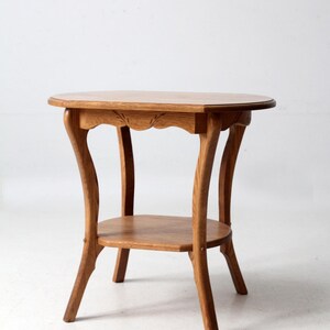 May include: A vintage wooden side table with a round top and a lower shelf. The table has curved legs and a light brown finish. The top edge features a decorative carved design. A classic piece of furniture.
