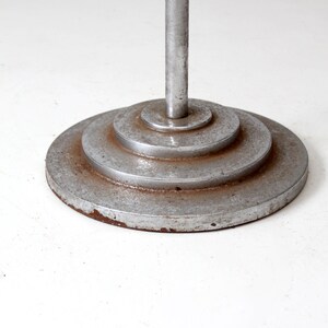 May include: A silver metal floor lamp base with a circular, tiered design. The base has a worn, aged appearance.