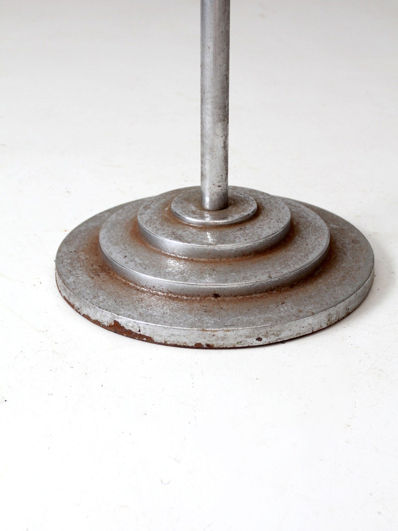 May include: A silver metal floor lamp base with a circular, tiered design. The base has a worn, aged appearance.