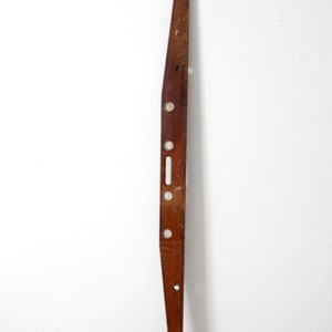 May include: A vintage wooden level with four bubble vials and metal hanging hooks. The level is brown and has a slightly curved shape.