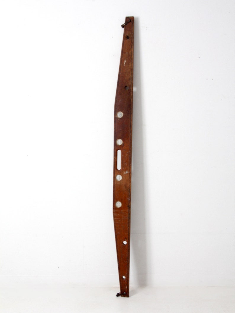 May include: A vintage wooden level with four bubble vials and metal hanging hooks. The level is brown and has a slightly curved shape.