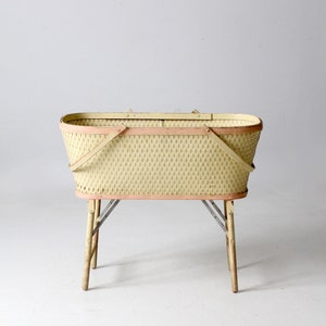 May include: A vintage wicker basket with a light yellow finish and pink trim. The basket has a folding handle and sits on four wooden legs.