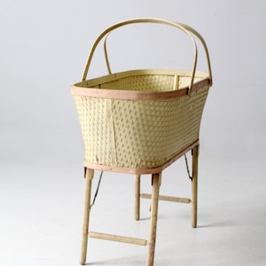 May include: A white wicker baby bassinet with a pink trim and folding legs. The bassinet has a handle on the top.