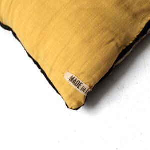 May include: A yellow throw pillow with black trim and a white label that says "MADE IN" on it.