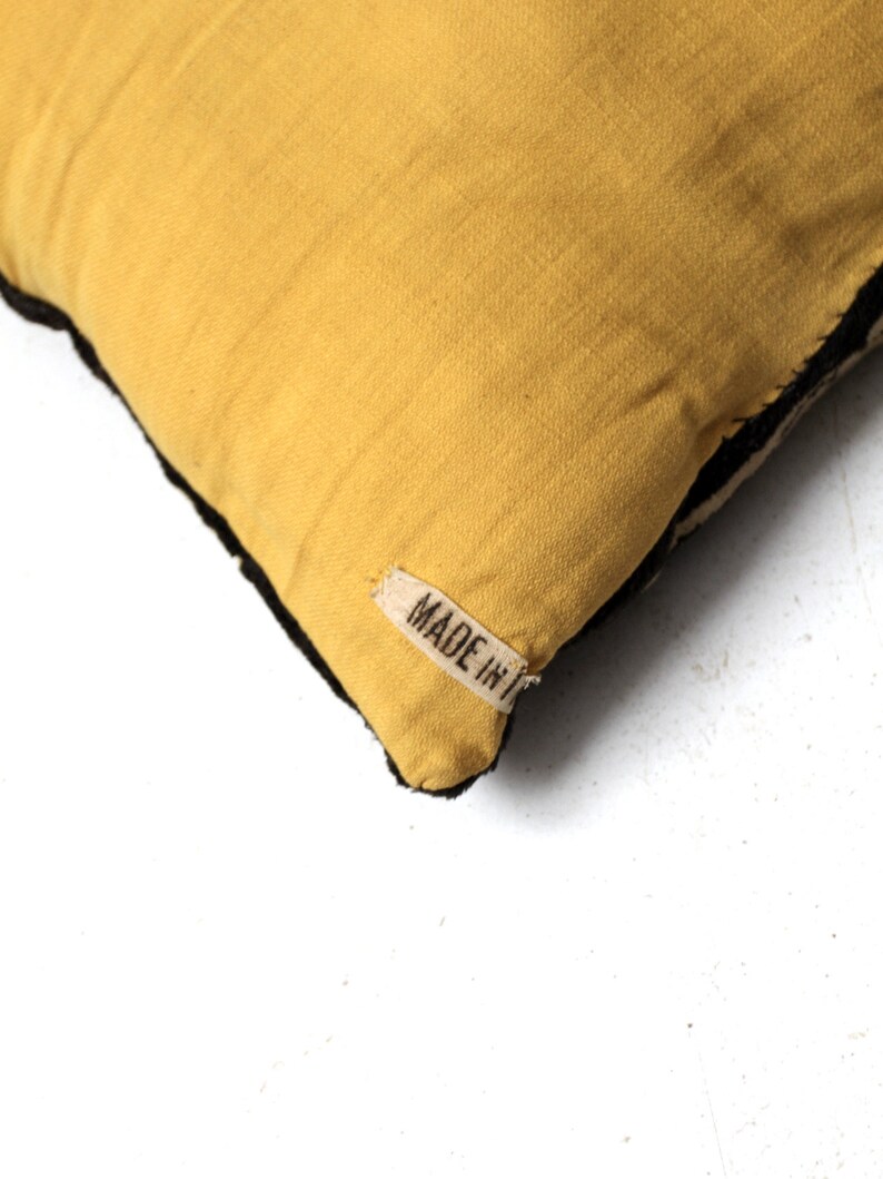 May include: A yellow throw pillow with black trim and a white label that says "MADE IN" on it.