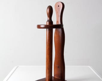 Könnte beinhalten: Ein Vintage-Toilettenpapierhalter aus Holz. Der Halter besteht aus dunkelbraunem Holz und verfügt über einen vertikalen Pfosten mit einem kleinen Regal und einer gebogenen Rückenstütze. Die Basis ist quadratisch und das Design ist einfach und funktional.