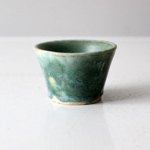 Peut inclure: Une petite tasse en céramique verte avec un bord légèrement évasé. La tasse a un glaçage marbré avec des nuances de vert et de blanc.