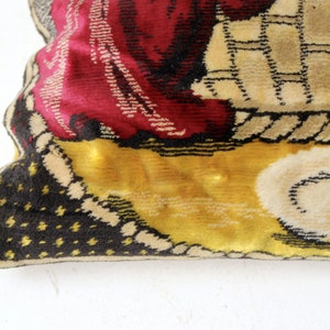 May include: A vintage tapestry pillow with a colorful design featuring a person in a red robe and a yellow background. The pillow has a black and white polka dot pattern on the back.
