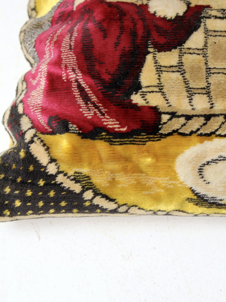 May include: A vintage tapestry pillow with a colorful design featuring a person in a red robe and a yellow background. The pillow has a black and white polka dot pattern on the back.