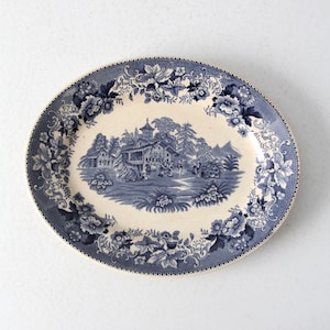 May include: Oval serving platter with a blue and white floral and landscape design. The center features a detailed scene of a building and figures. The rim is decorated with floral patterns. A classic piece for serving food.