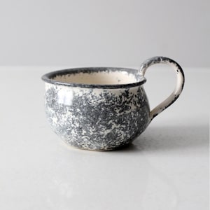 Puede incluir: Una taza de cerámica blanca con un esmalte gris moteado y una asa redondeada.