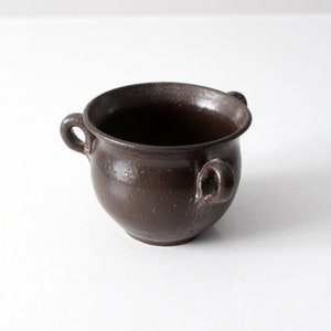 以下が含まれることがあります： 2つの取っ手が付いた、小さな茶色の陶器の壺。壺は丸く、滑らかでマットな仕上がりです。