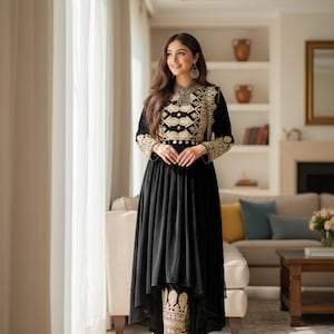 May include: A black dress with gold embroidery on the bodice and cuffs. The dress has a high-low hemline and is paired with matching embroidered pants. The outfit is accessorized with silver jewelry.