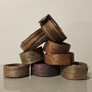 以下が含まれることがあります： 茶色と紫色の木製リングの積み重ね。リングは薄い木のストリップで作られており、木目がはっきりと見えます。リングは積み重ねられており、小さな塔を形成しています。